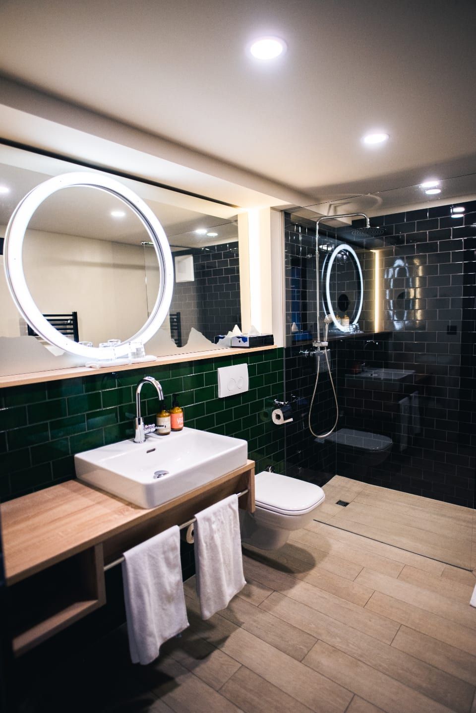 Modern bathroom with dark green tile, a white sink and a round lit mirror
